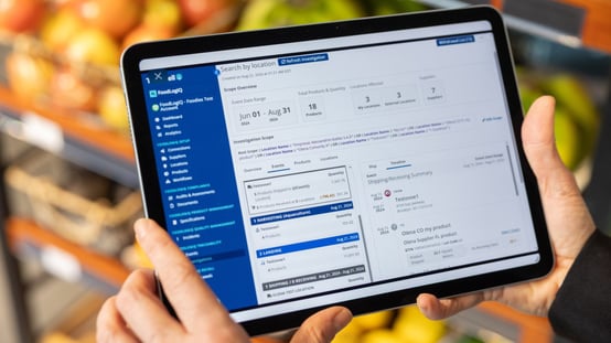 Person holding a tablet displaying a food traceability software dashboard with product, location, supplier and shipping data.